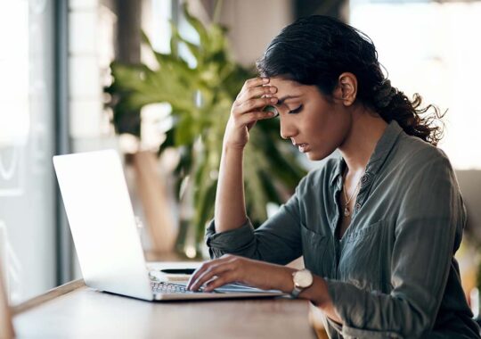 Woman at laptop looking tired and rubbing at her forehead in mental exhaustion