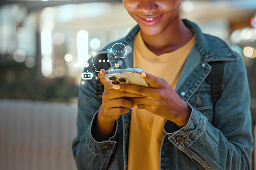 Happy young African American woman using mobile smartphone with AI chatbot for online information in night town